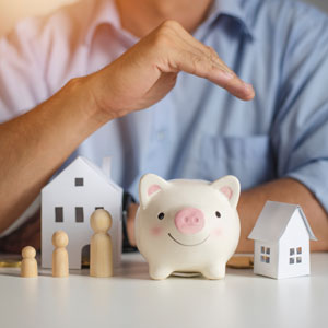 Hand protecting piggy bank and wooden figures, symbolizing asset protection and wealth planning
